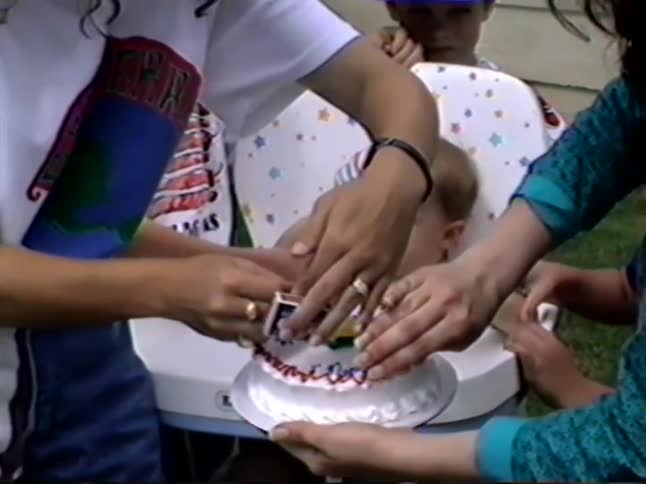 A baby cries during the chaotic lighting of his first birthday candle before happily clapping for his cake in this vintage home video