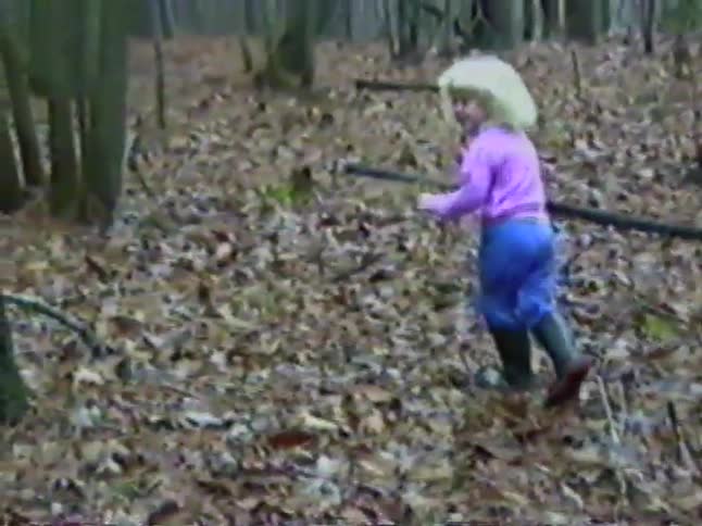 Vintage VHS footage shows a little blonde girl in a pink shirt walking through a forest covered in autumn leaves