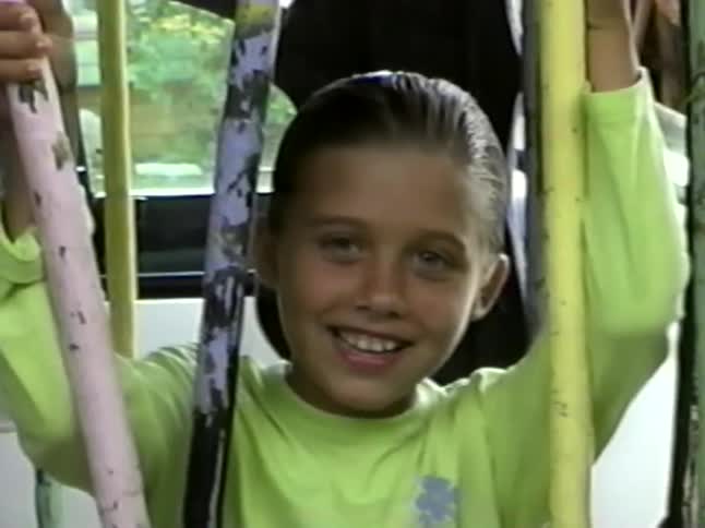 A smiling young girl with slicked-back wet hair looks at the camera in this vintage-style footage