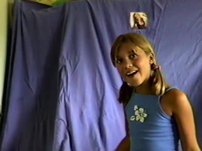 Young girl performs and gestures energetically in front of a blue fabric backdrop indoors