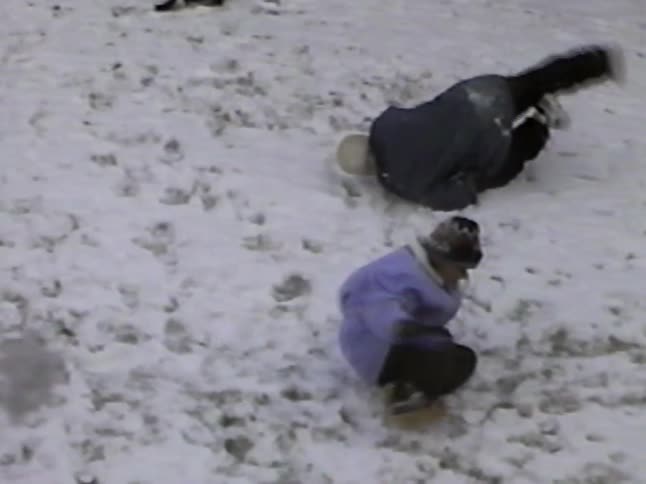A mother and child playfully wrestle and have a snowball fight in a snowy backyard in this vintage home video