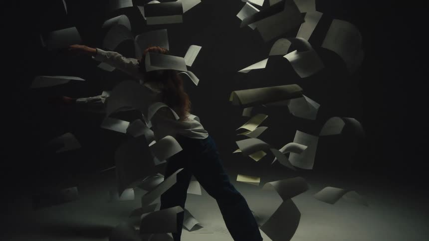 Cinemagraph of a woman standing in a dramatic pose as papers float around her in slow motion