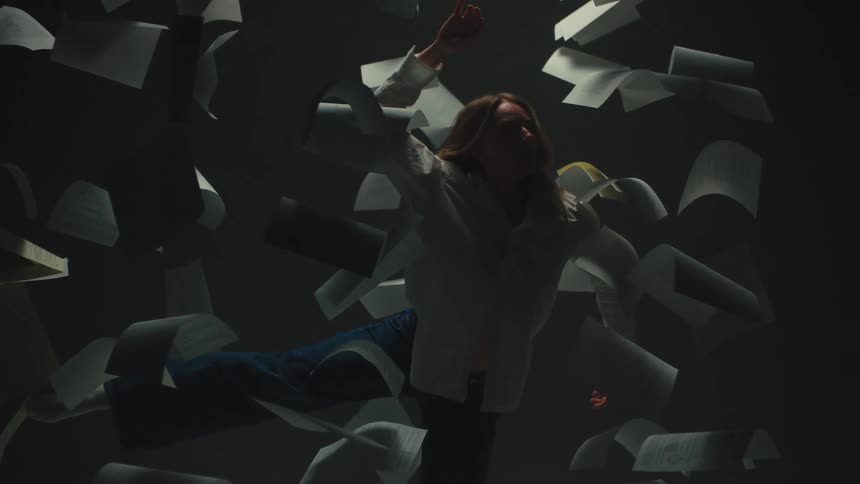 A surreal, slow-motion scene shows a woman falling through a dark space as papers float around her