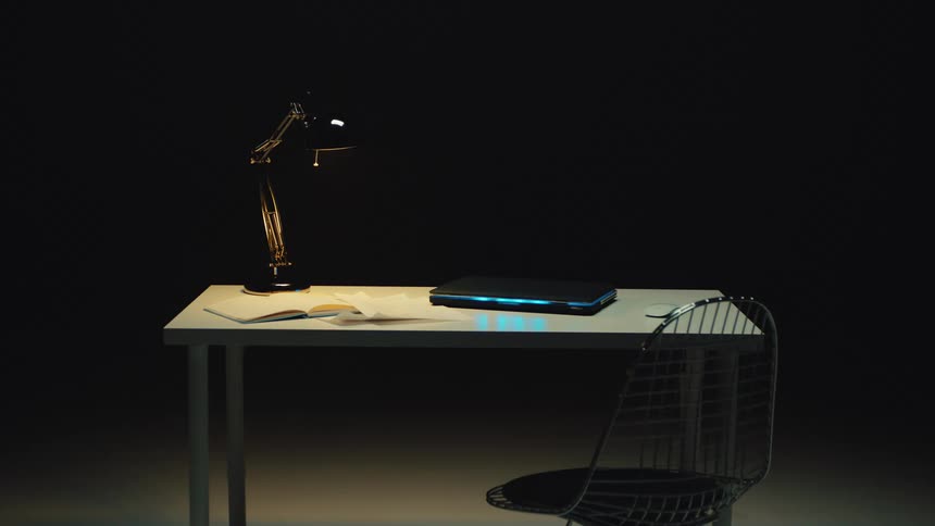 Minimalist workspace with a glowing laptop and desk lamp set against a black background in a seamless loop