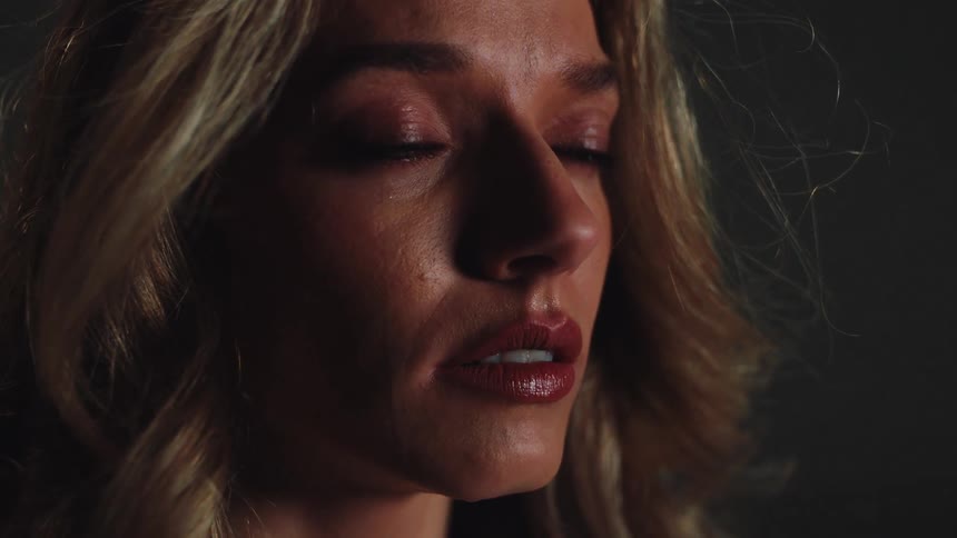 A slow-motion close-up captures a single tear on the cheek of a beautiful, sad woman with blonde hair as she closes her eyes in despair