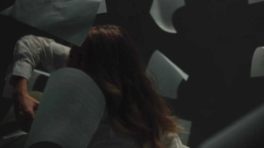 An overwhelmed woman appears lost and stressed as she is surrounded by a whirlwind of falling papers in slow motion