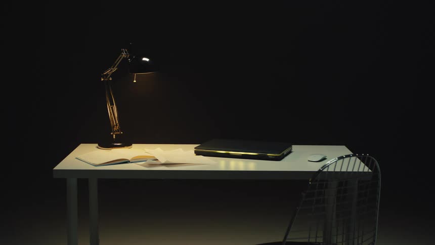 A modern, minimalist workspace with a lit lamp sits empty in a dark room