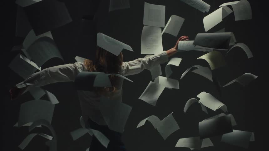 A woman dances in slow motion, her body weaving through a chaotic storm of suspended paper sheets in a dark studio