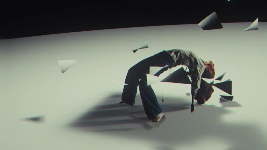 A dancer contorts her body backwards in slow motion as paper objects float around her in a minimalist, surreal studio setting