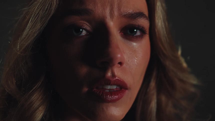 An intense close-up shot of a distraught young woman's face with a tear on her cheek in a dark room