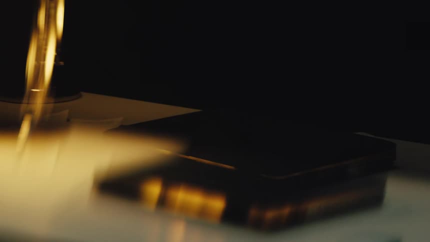 Moody close-up rack focus of a closed laptop resting on a desk under the warm glow of a lamp at night