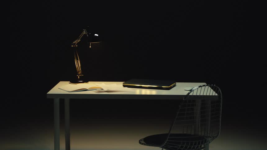 An empty modern workspace is illuminated by a single lamp against a black background