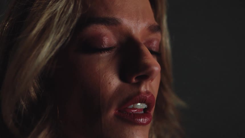 A dramatic close-up in slow motion shows a tear rolling down the cheek of a heartbroken woman with her eyes closed