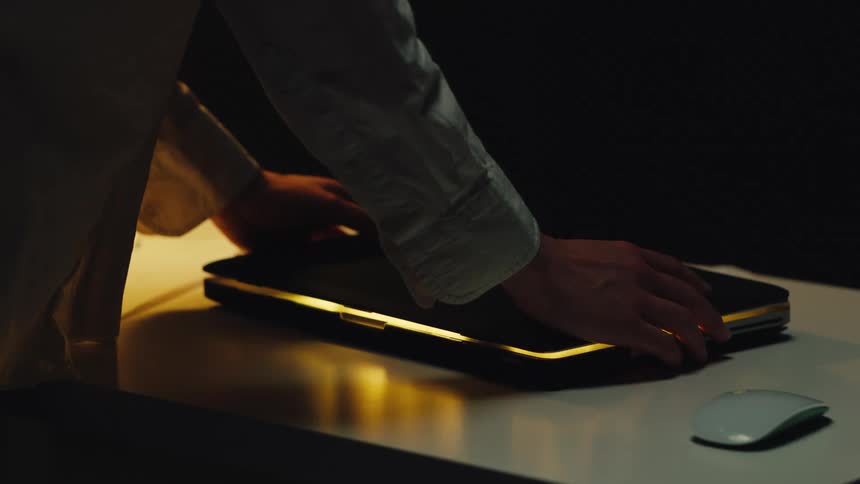 Cinemagraph of a warm light pulsing from a closed laptop computer on a desk in a dark room