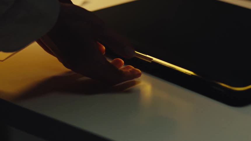 Close up of silhouetted hands nervously hovering over a glowing, slightly open laptop in a dark, moody room