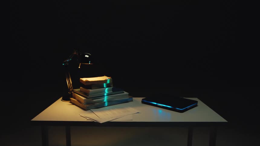 A futuristic blue scanner analyzes a stack of old books and a laptop on a desk in a dark, lamp-lit room