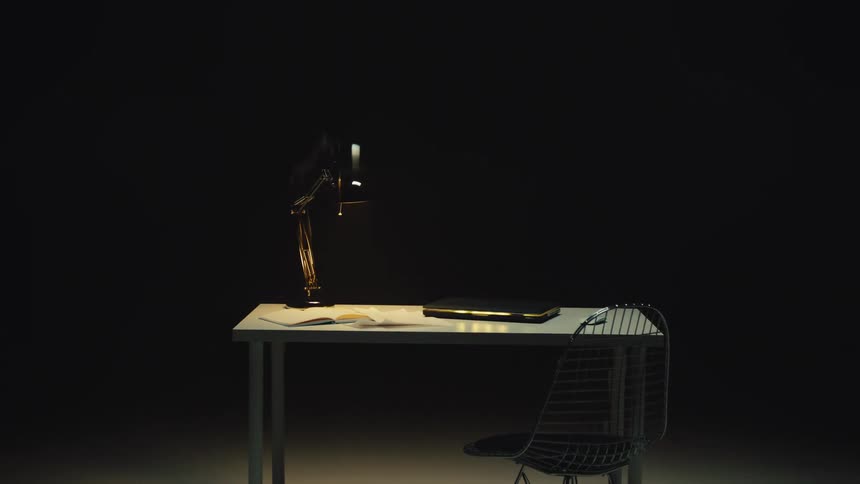 A modern, minimalist desk with a lamp and book vibrates and shakes with a glitch effect in a dark room