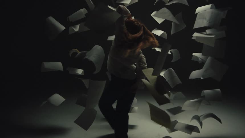 A woman gracefully moves in super slow motion as papers fly around her in a dramatically lit studio