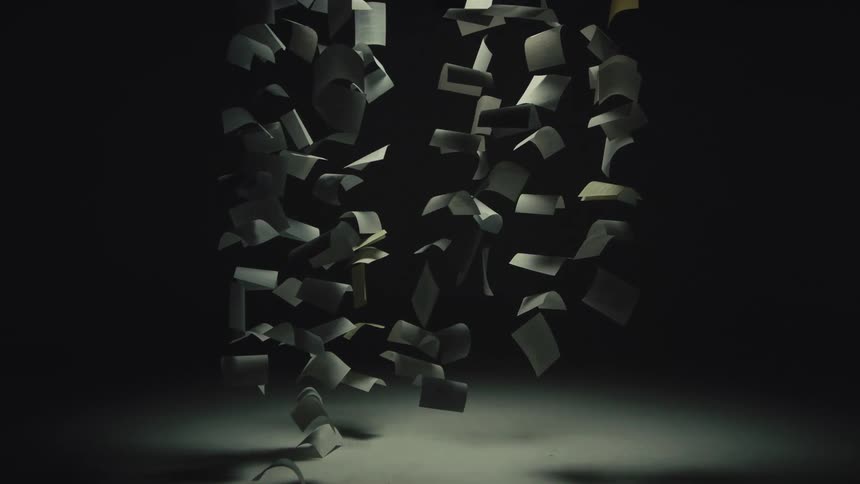 Artistic slow motion shot of countless pieces of paper falling against a dark, spotlit background
