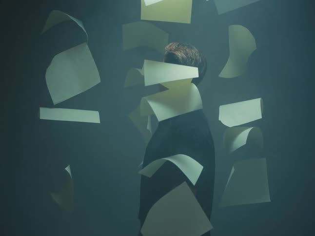 Surreal cinemagraph shows a man turning away from the camera as sheets of paper float around him in a smoky room