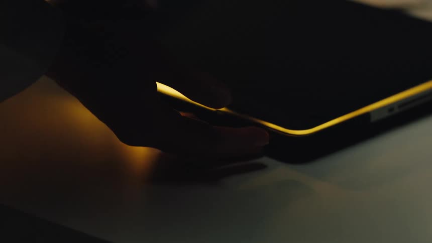 A person's hands slide across and interact with a futuristic, glowing digital tablet in a dark room before removing a stylus
