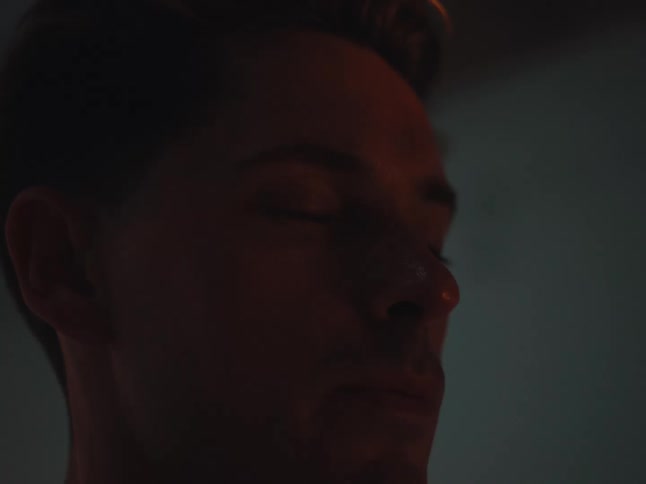 Close up on a contemplative man's face as a warm light passes over, and he slowly opens his piercing blue eyes