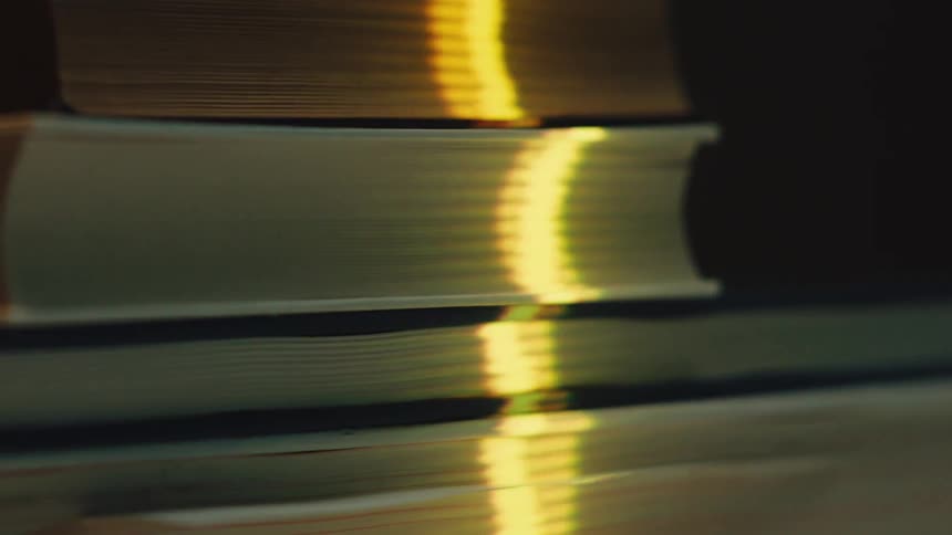 A warm golden light shimmers and reflects across the pages of a stack of books in a dark setting