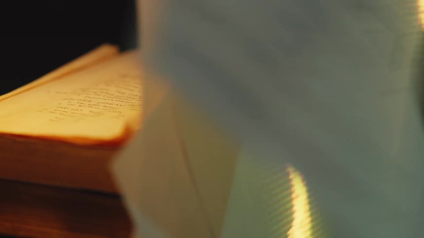 An abstract waveform of golden light is projected onto the pages of a book as they turn in slow motion