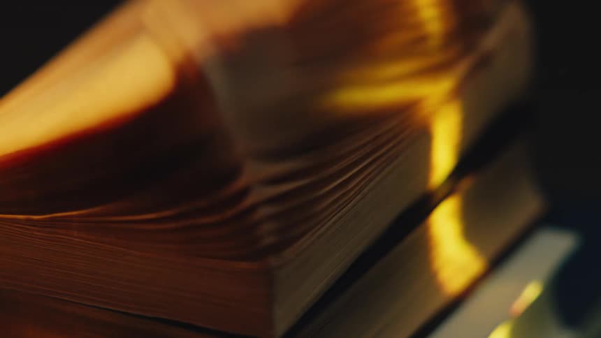 The pages of an old book turn quickly in the warm, dramatic light against a dark background