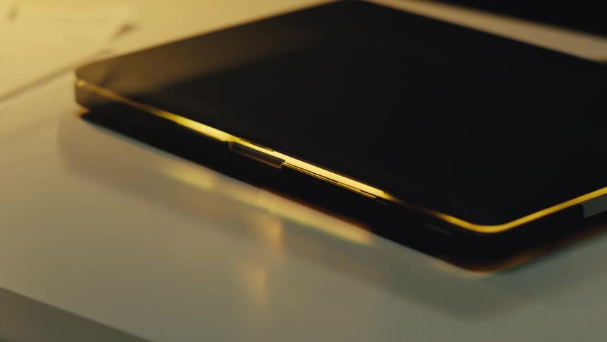 Light flickers and pulses from the screen of a closed laptop resting on a desk in a dark room