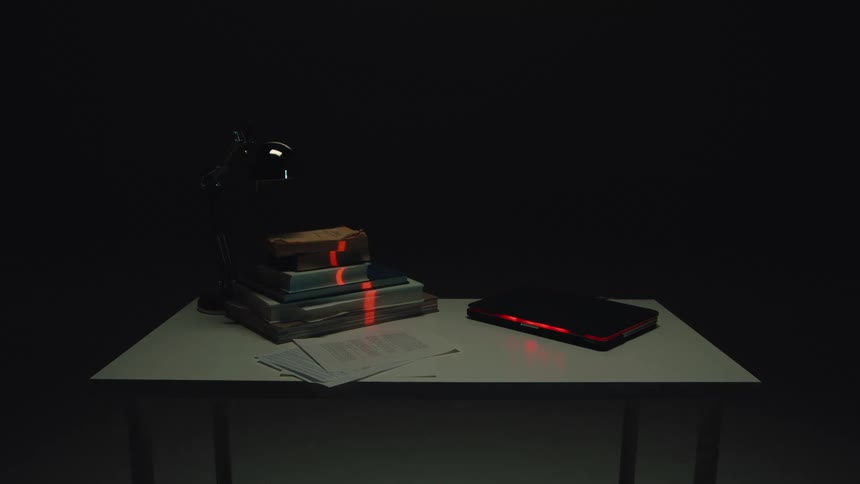 A red laser from a futuristic device scans a stack of old books and papers on a desk in a dark room
