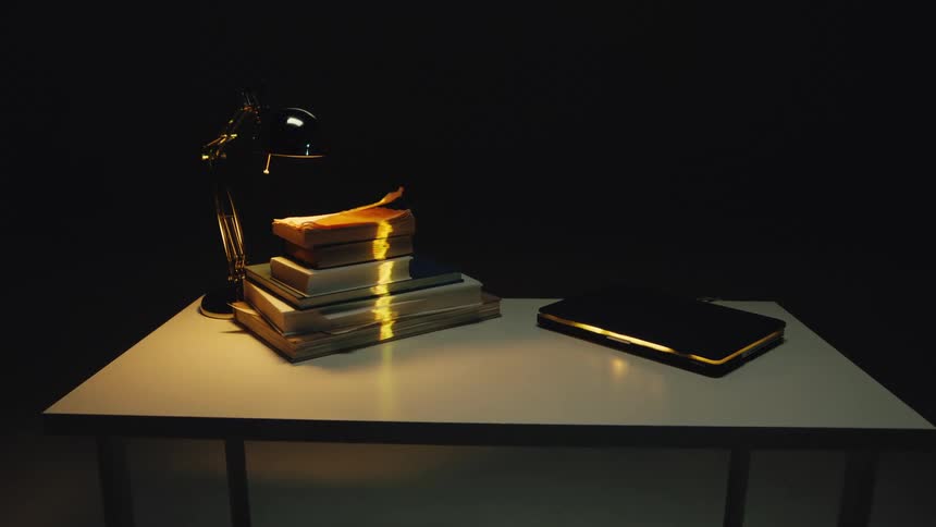 In a dark and mysterious room, papers fly chaotically around a desk lamp illuminating a glowing stack of books