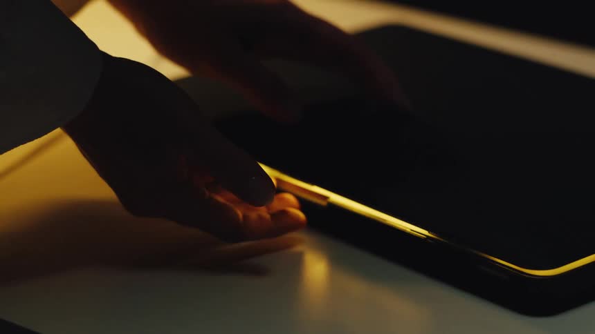 Close up of a person's hands slowly closing a laptop in a dark room as the screen's warm light fades out