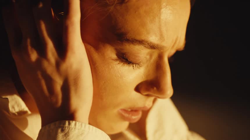 Close up on the face of a troubled woman in distress, holding her head with her hands in dramatic lighting