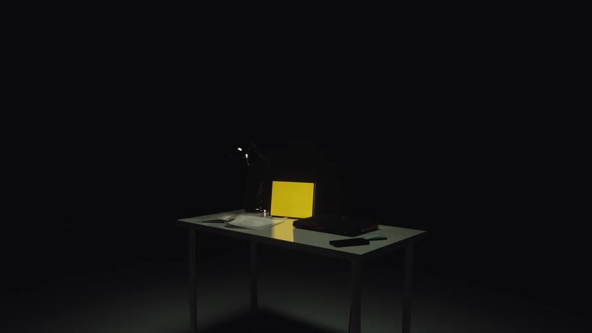A modern desk in a dark room is illuminated by a single spotlight as the screens of a laptop, tablet, and smartphone glow yellow