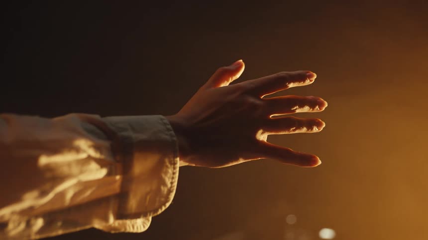 A close-up of a person's hand reaching out, illuminated by a warm, golden light against a dark, smoky background
