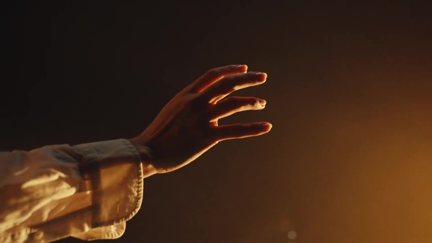 An arm extends into a warm, golden spotlight, and the hand slowly curls into a rock-and-roll sign in slow motion