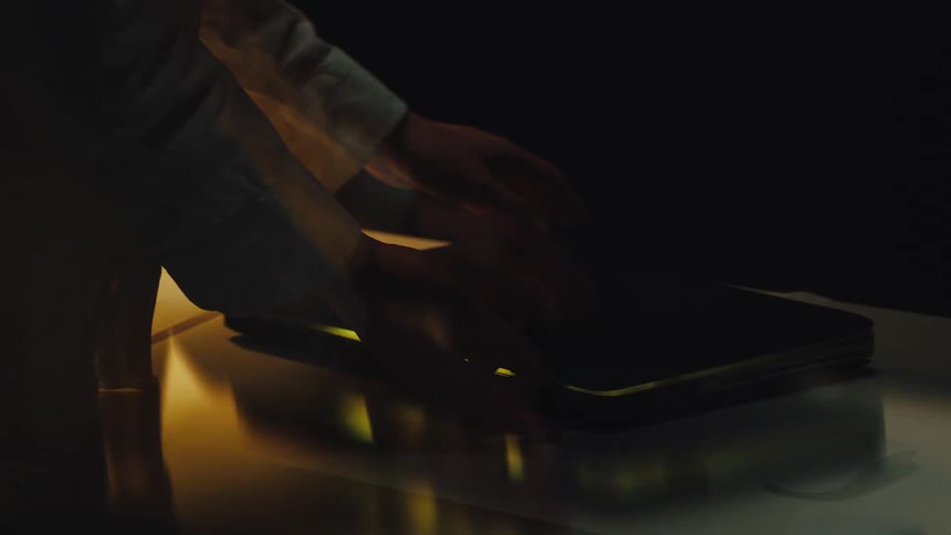 A stressed and overworked person slowly closes their laptop late at night in a dark room, with motion blur effects indicating exhaustion