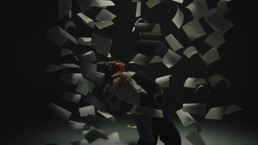 A woman arches backward in a dramatic pose as sheets of paper fall around her in super slow motion
