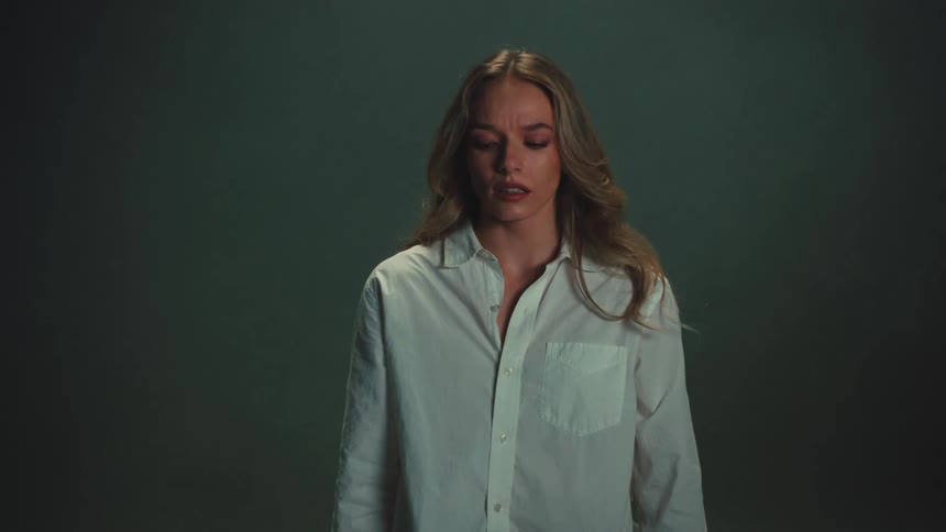 A somber woman with a worried expression watches a medical mask fall in slow motion