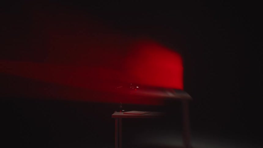 A projector on a table emits a beam of red light into a dark, smoky room