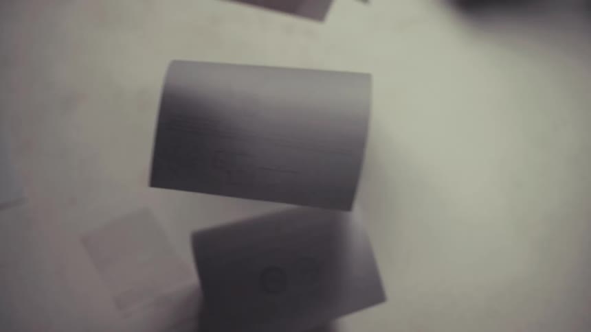 An artistic, out-of-focus close-up shot of papers with text and drawings hanging by threads and slowly swaying
