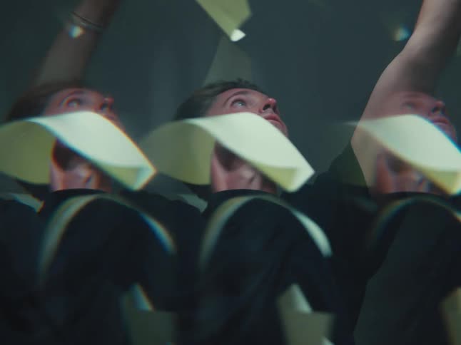 A man looks up with a bewildered expression as papers fall all around him, viewed through a dreamy kaleidoscope lens