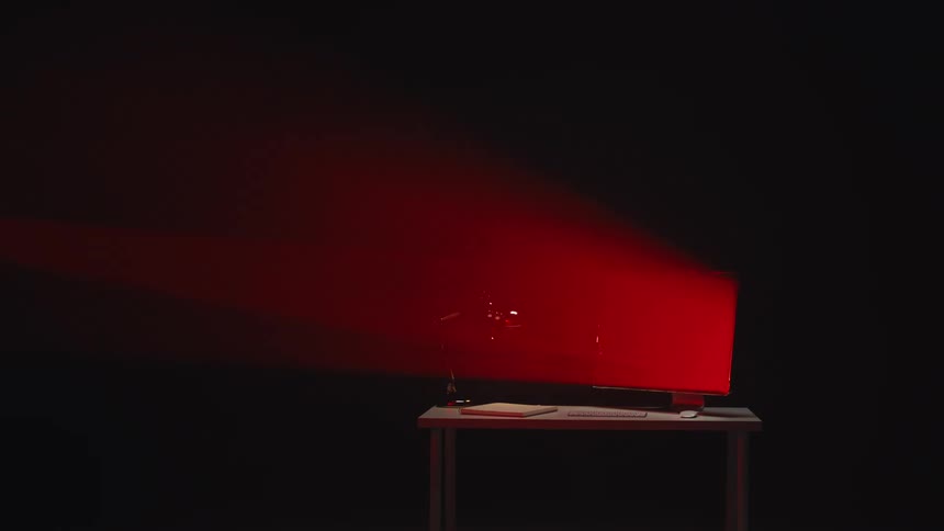 An empty workstation with a computer and lamp is dramatically lit by a red spotlight in a black studio