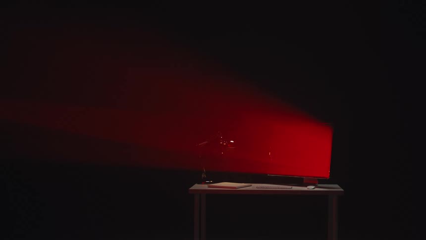 Dramatic slow motion shot of a desktop monitor on a table exploding under a red light in a dark room