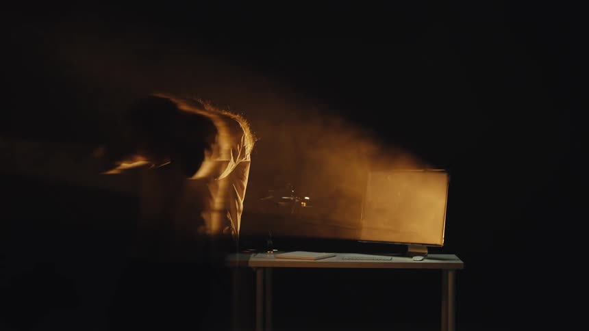 A dramatic long exposure shot captures a person's psychological breakdown in a dark room, illuminated only by the glow of a computer monitor