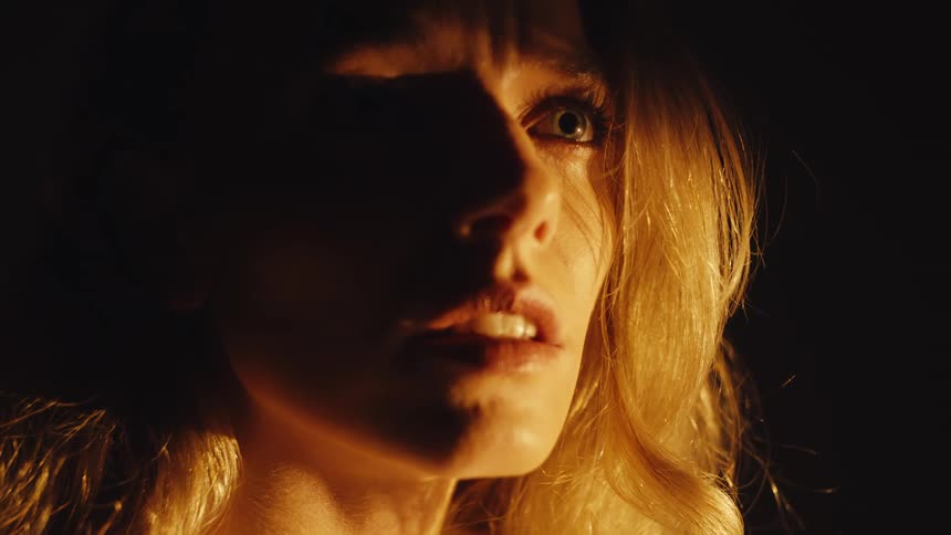 A dramatic close-up of a terrified woman's face illuminated by a flickering light in the darkness