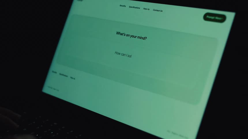 A person types a question into an AI chatbot on a laptop computer screen in a dark room