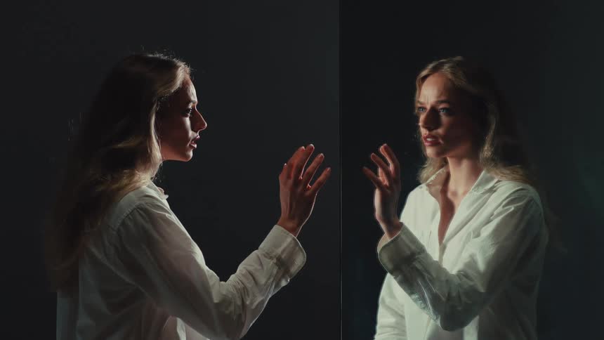Cinemagraph of a lonely woman in a dark room slowly touching her reflection in the mirror