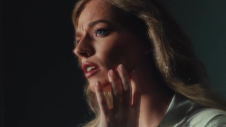 A horrified young woman with a terrified expression touches her face in slow motion